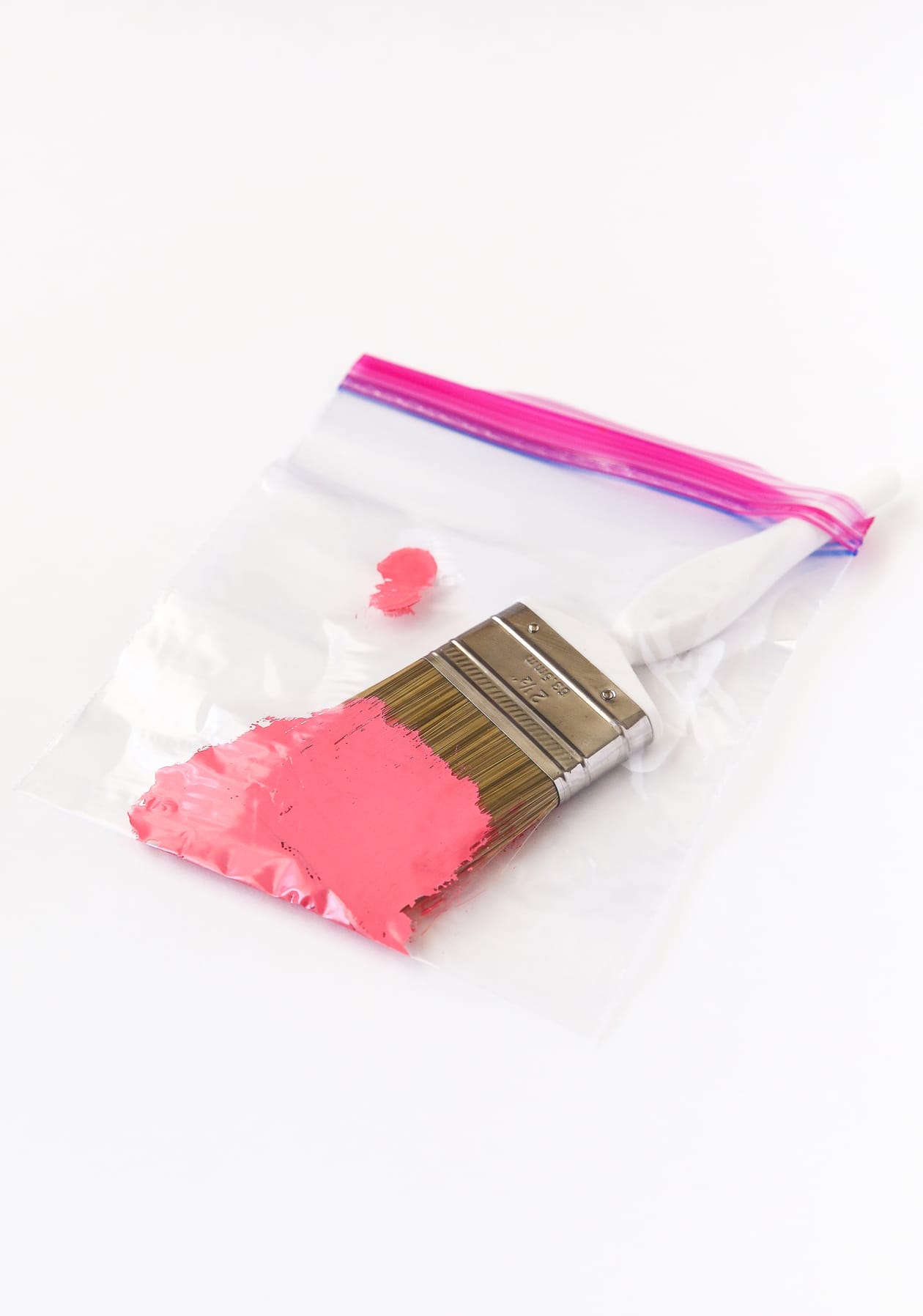 Paint brush with pink paint being used to paint wooden chairs